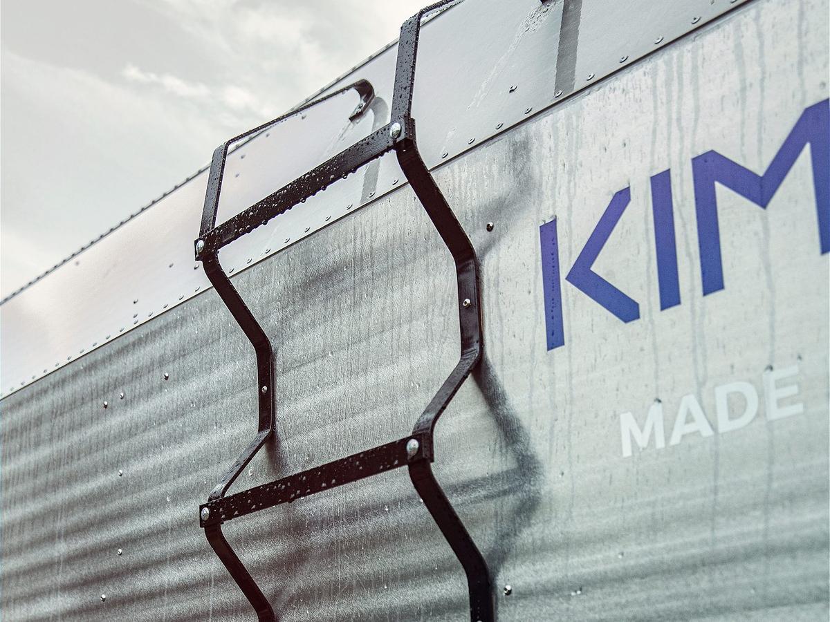 KIMBO Made in USA wordmark on the corrugated aluminum sidewall of a Kimbo truck bed camper, with the integrated black side ladder mounted to hand-riveted aluminum panels in close-up detail.