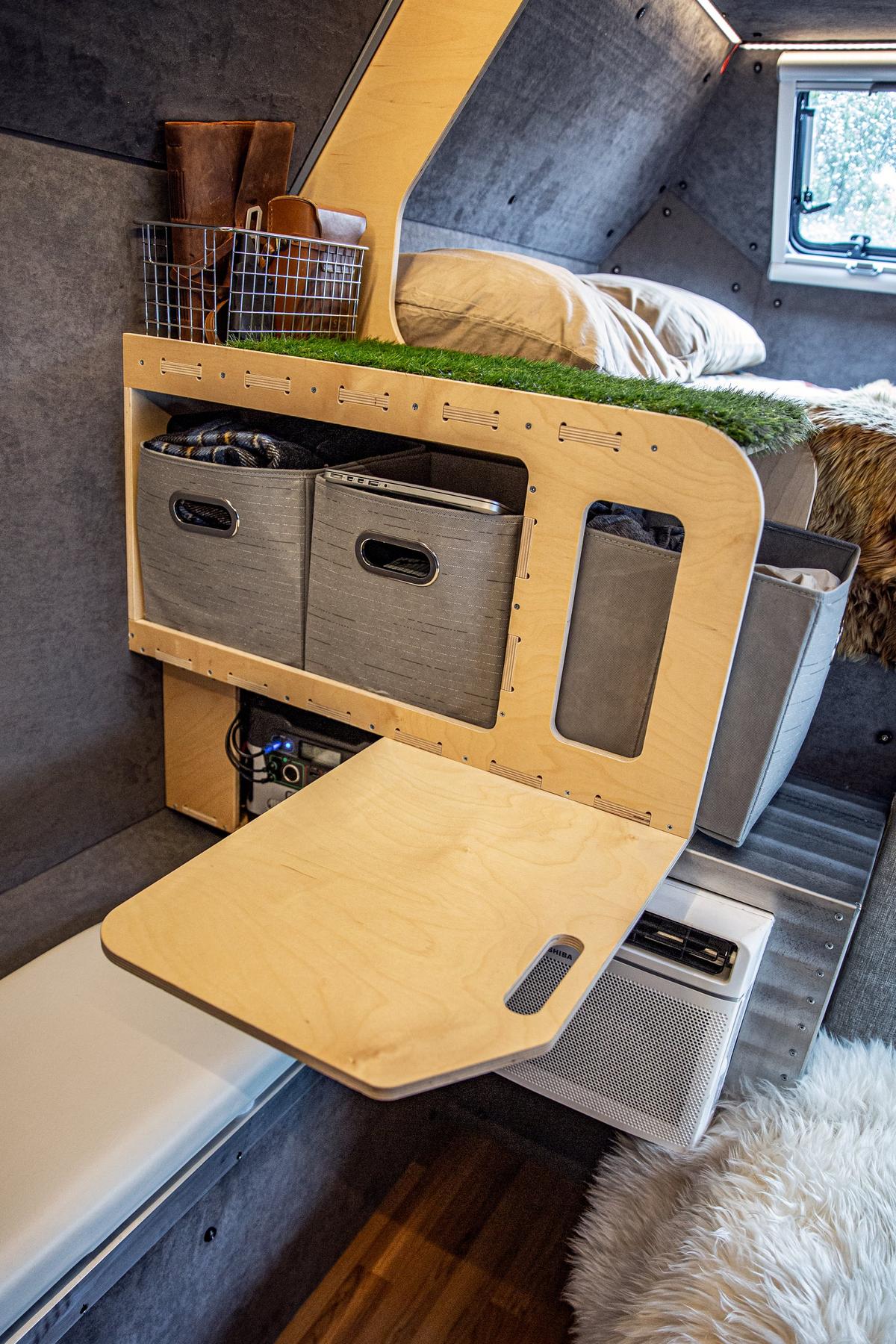 Plywood mudroom storage area inside a Kimbo 6 hard-side aluminum truck bed camper, hand-stitched leather boots in a side basket, fabric storage bins below, fold-down step seat extended, sheepskin throw visible on the bed at right.