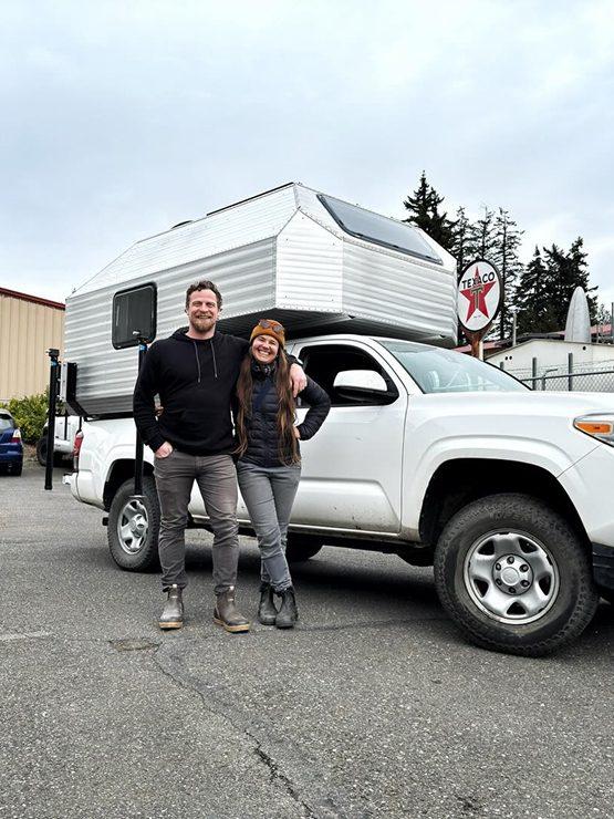 Kimbo owner Sam Kim and his partner standing in front of his white pickup with a freshly-installed Kimbo hard-side aluminum truck bed camper at the Bellingham, Washington factory delivery.